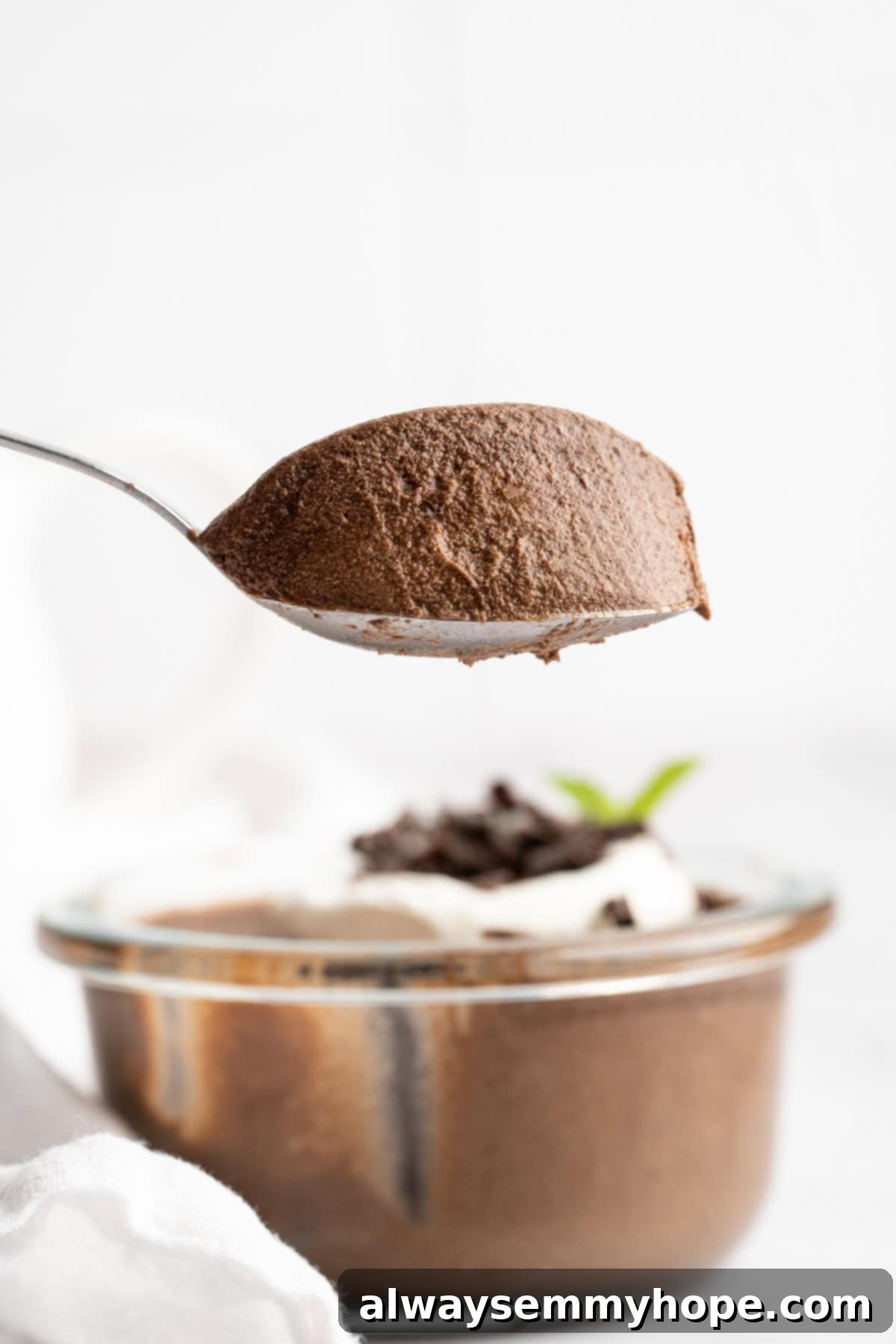 This Chocolate Avocado Pudding is ultra rich and decadent, with the creamiest texture and deepest chocolate flavour. Just 10 minutes of prep! A spoon lifts a generous scoop of thick, creamy, and dark chocolate avocado pudding from a bowl, showcasing its smooth texture and rich color.