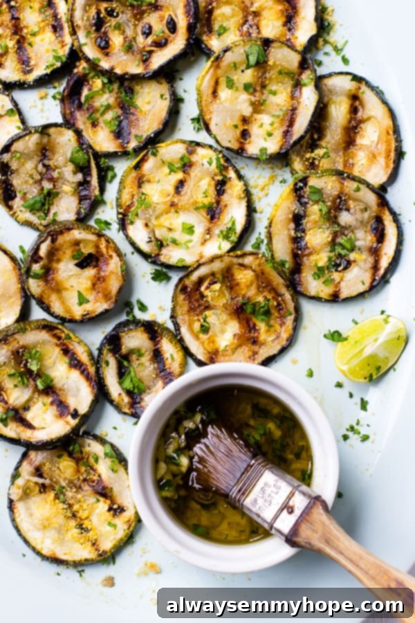 Closeup view of glistening lemon garlic grilled zucchini slices artfully arranged on a platter, with a small bowl of marinade and a brush for emphasis.