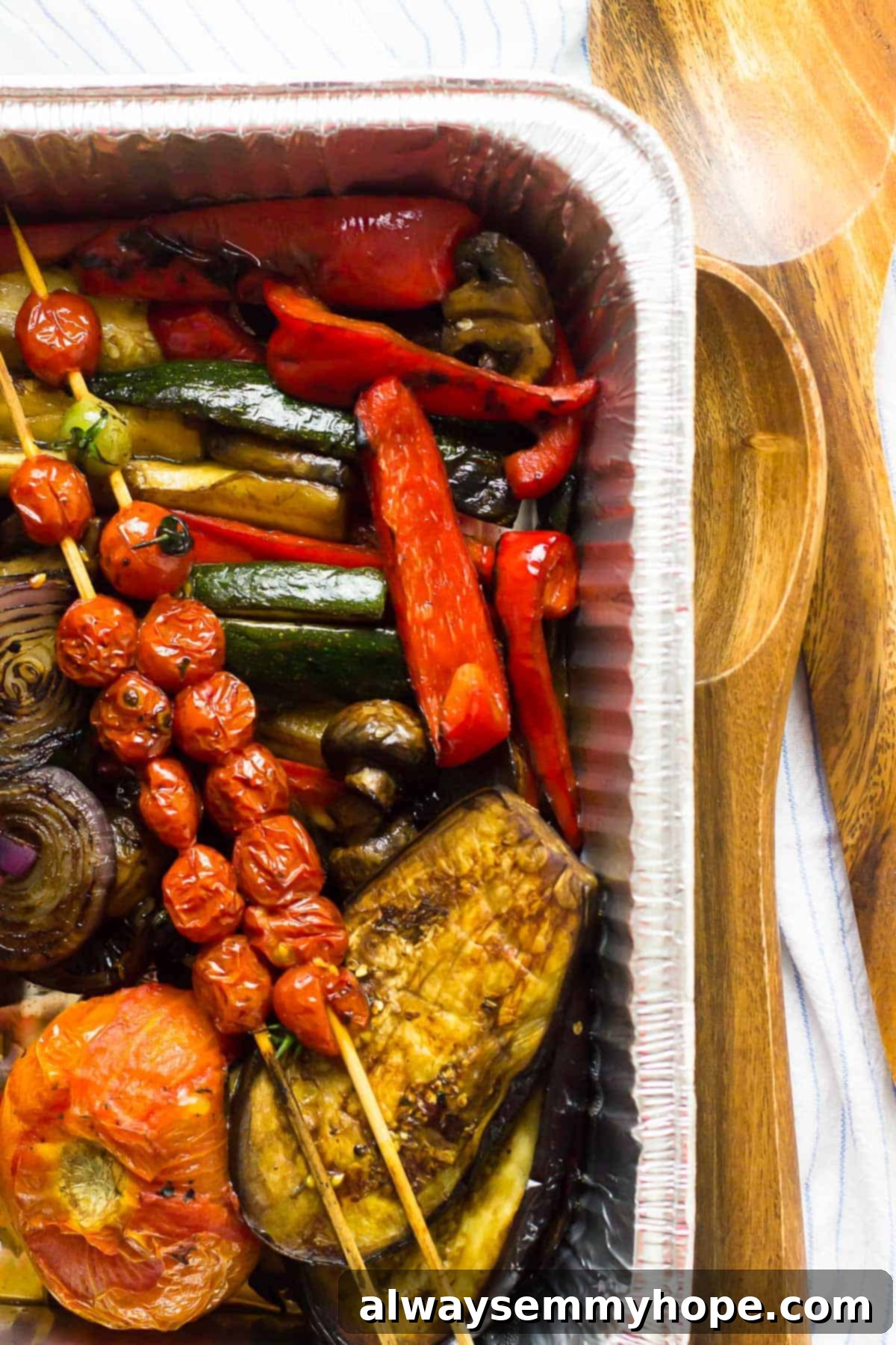 Grilled vegetables in a foil pan with wooden servers on the side