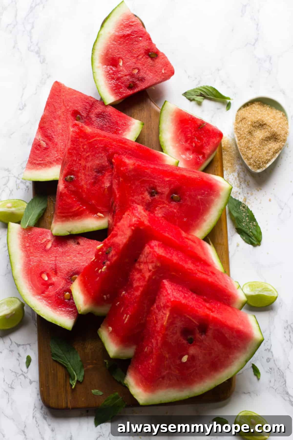 Wedges of watermelon on cutting board with lime wedges and mint leaves