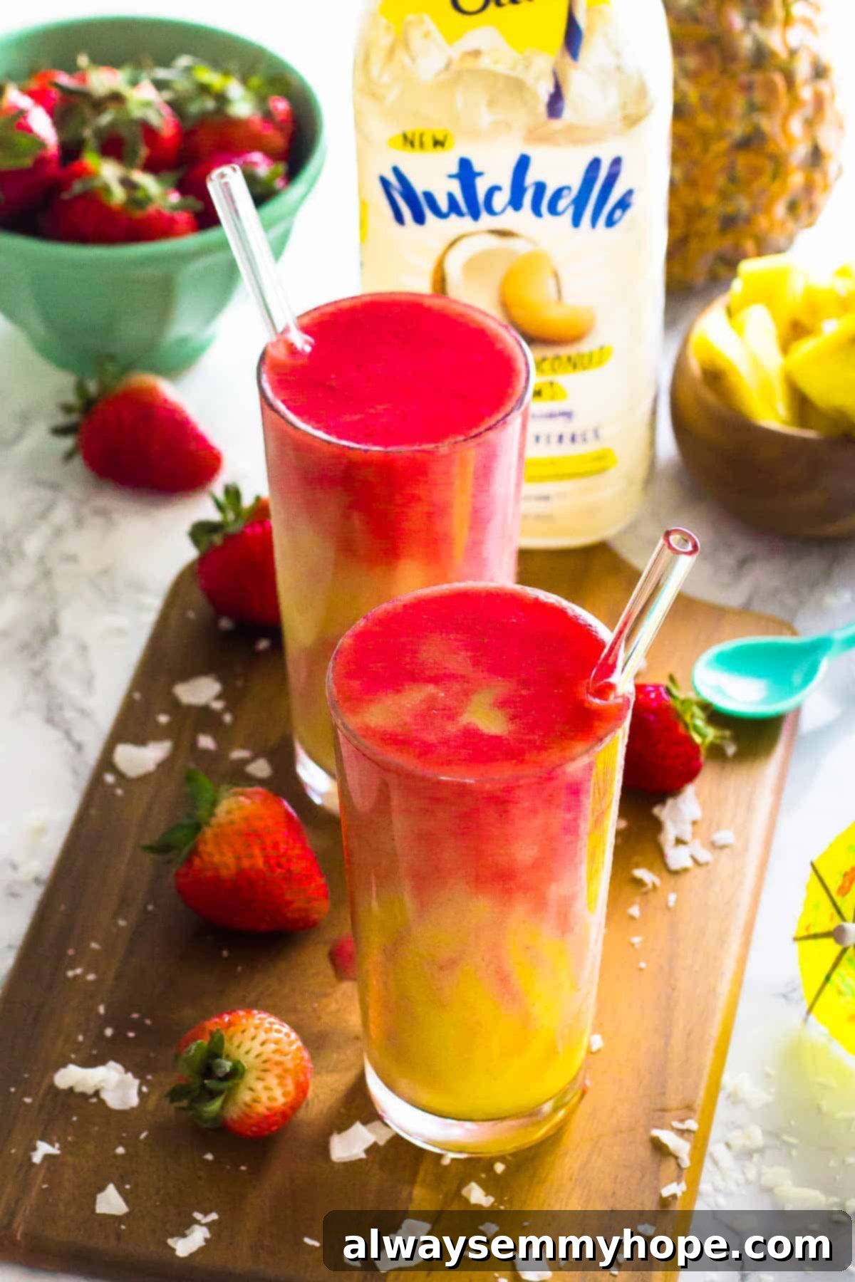 Two strawberry pineapple coconut smoothies in tall glasses with strawberries on the side. This Lava Flow Smoothie is loaded with delicious spring and summer fruits and bound to be your new favourite smoothie!