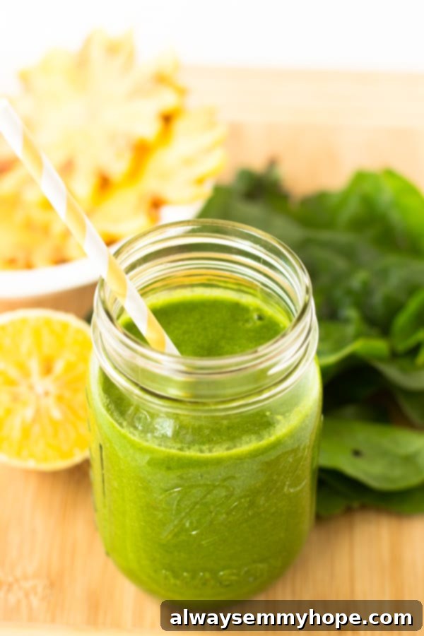 A tropical green smoothie in a mason jar with a yellow straw, featuring bright citrus flavors.