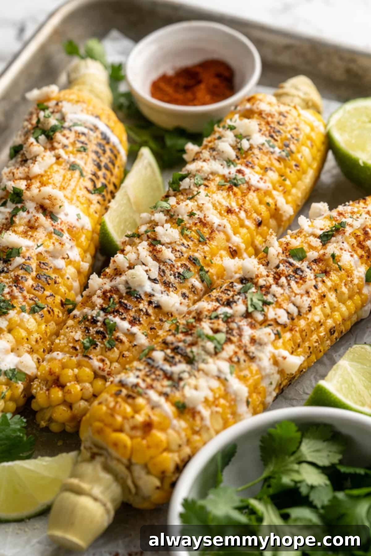 Garnished Vegan Elotes with Extra Toppings. Vegan Elotes on a sheet pan, surrounded by small bowls of chili powder, fresh cilantro, and lime wedges, emphasizing garnish options.