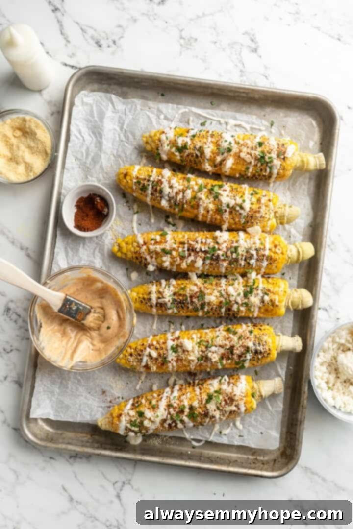 Assembling the Vegan Elotes Toppings. Overhead view of Mexican street corn on a sheet pan with a bowl of mayo mixture ready to be applied.