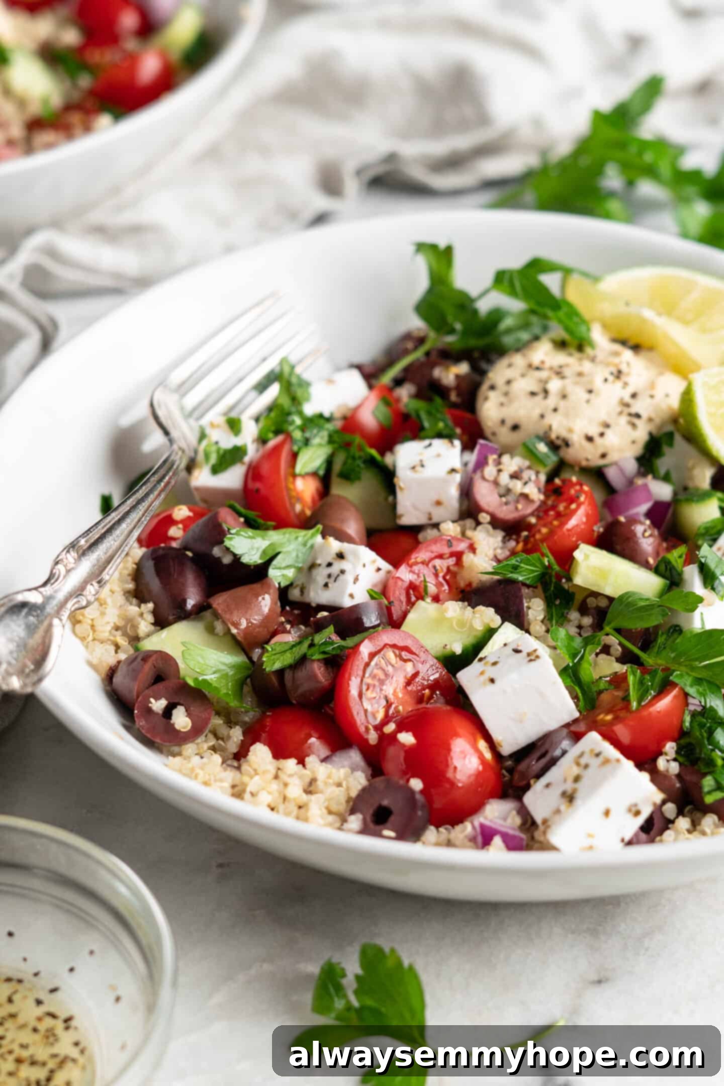 This easy Greek cucumber salad is loaded with filling veggies, topped with creamy hummus, and comes together in just 20 minutes! A white bowl with cucumber salad.