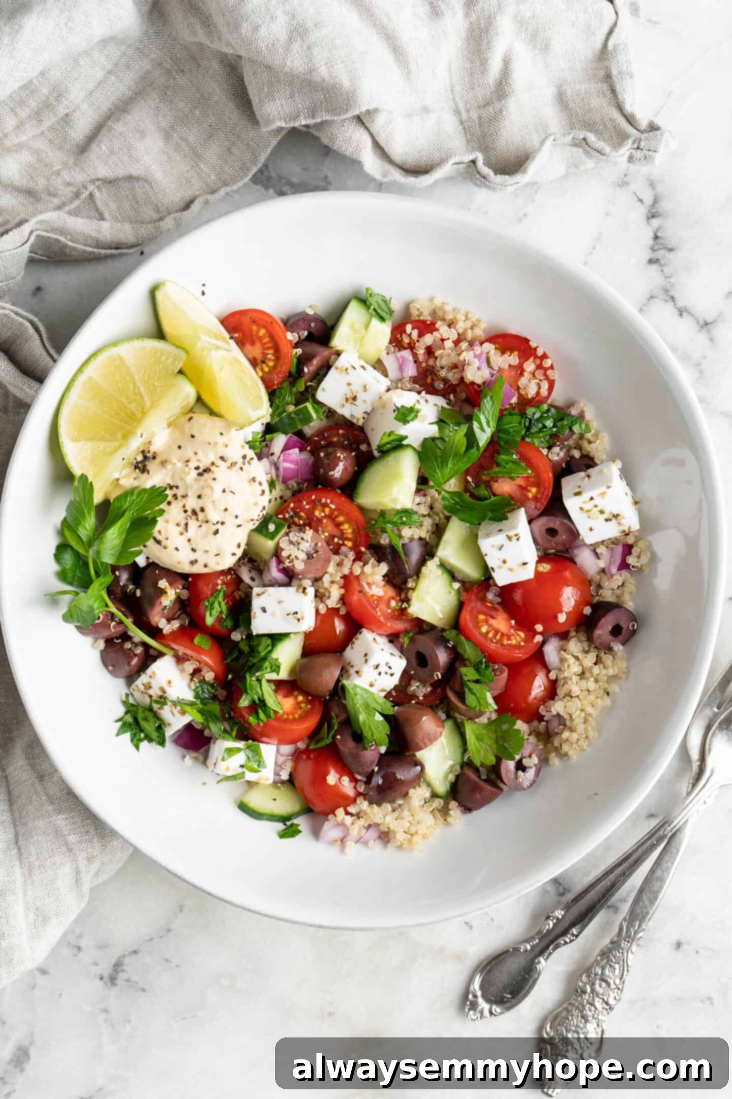 This easy Greek cucumber salad is loaded with filling veggies, topped with creamy hummus, and comes together in just 20 minutes! A white bowl with Mediterranean salad.