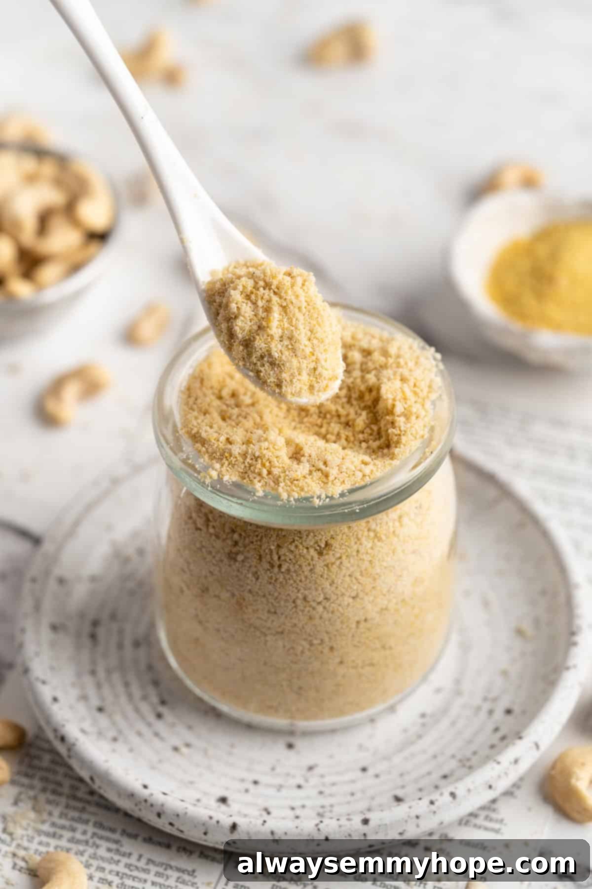 A spoon lifting a serving of homemade vegan Parmesan cheese from a jar, showing its crumbly texture.