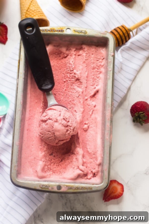 A tub of luscious vegan strawberry coconut ice cream with a scoop ready to serve.