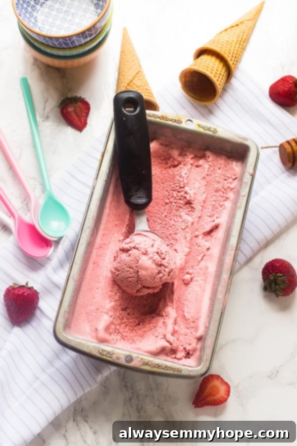 Overhead view of vegan strawberry coconut ice cream in a tub, with a scoop resting on top, garnished with fresh strawberries.