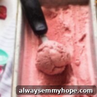 Vegan strawberry ice cream being scooped from a tub, ready to serve.