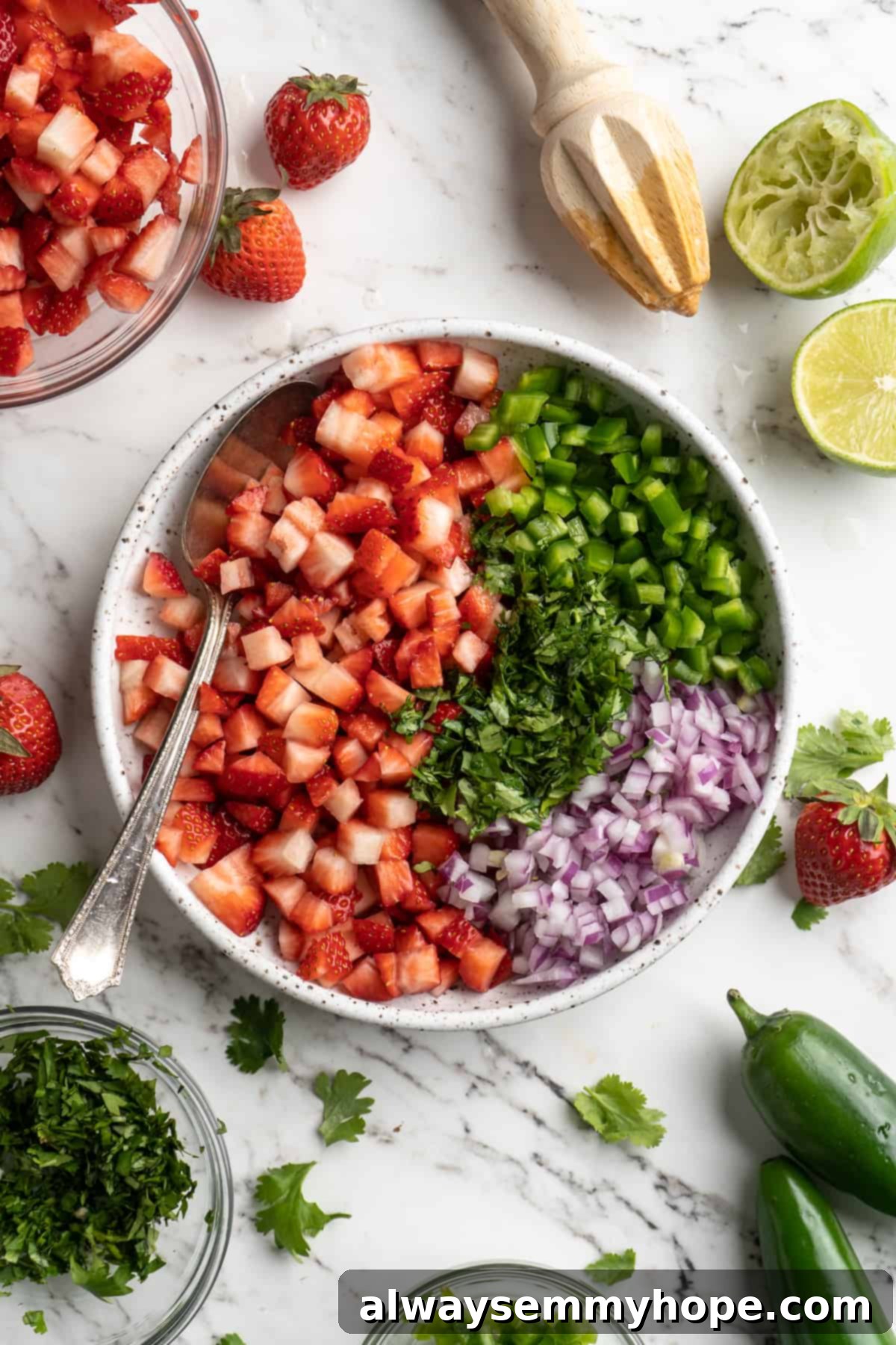 This 5-ingredient strawberry salsa takes only 10 minutes to make! It's a fresh, sweet, and spicy homemade salsa perfect for parties! Overhead view of ingredients for strawberry salsa in bowl with spoon