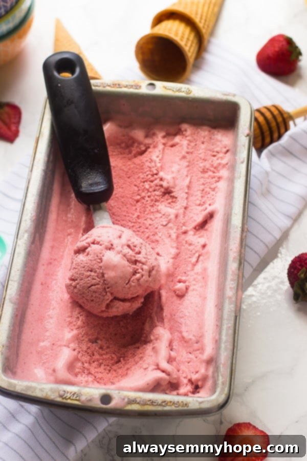 A big tub of vegan strawberry coconut ice cream with a scoop on top, garnished with fresh strawberries.