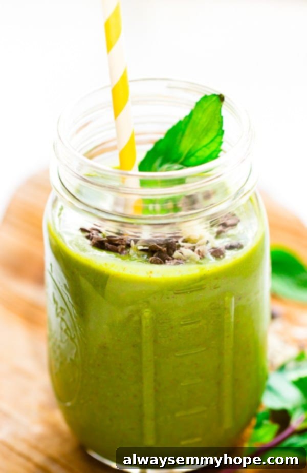 Mint Chocolate Chip Green Dream Smoothie 3 A close-up shot of a mint chocolate chip green smoothie in a clear mason jar, featuring a bright yellow straw, highlighting the rich green color and tempting texture.