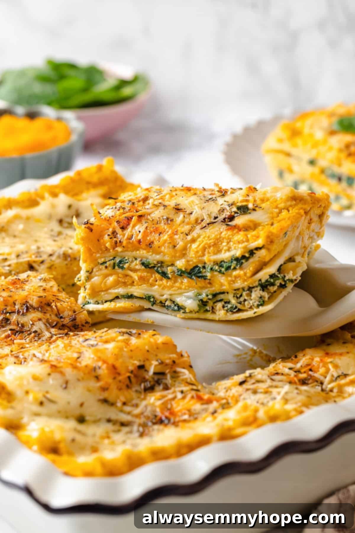 Spatula lifting a slice of butternut squash lasagna from a casserole dish, showcasing the layers of creamy squash, spinach ricotta, and vegan cheese.