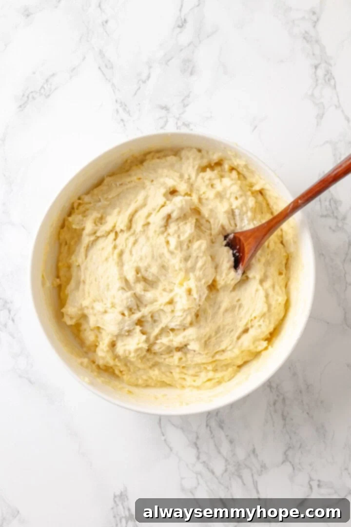 Vegan monkey bread dough being mixed in a bowl with a wooden spoon, showing the initial stages of dough formation.