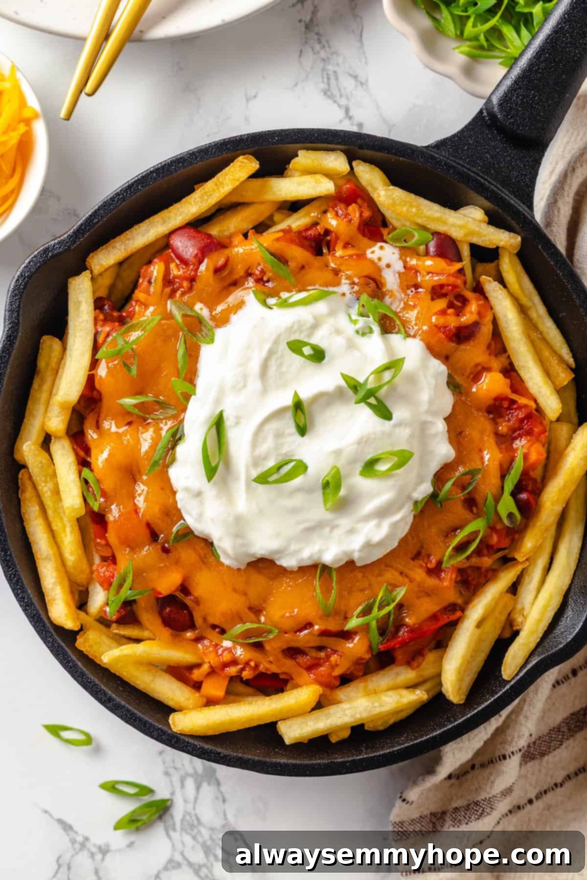 Skillet of vegan chili cheese fries topped with sour cream and green onions