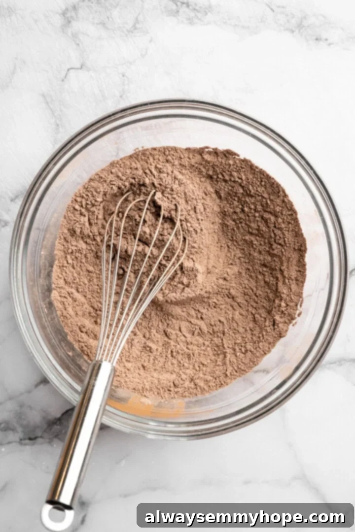 Dry ingredients for chocolate peppermint cookies in glass bowl with whisk.
