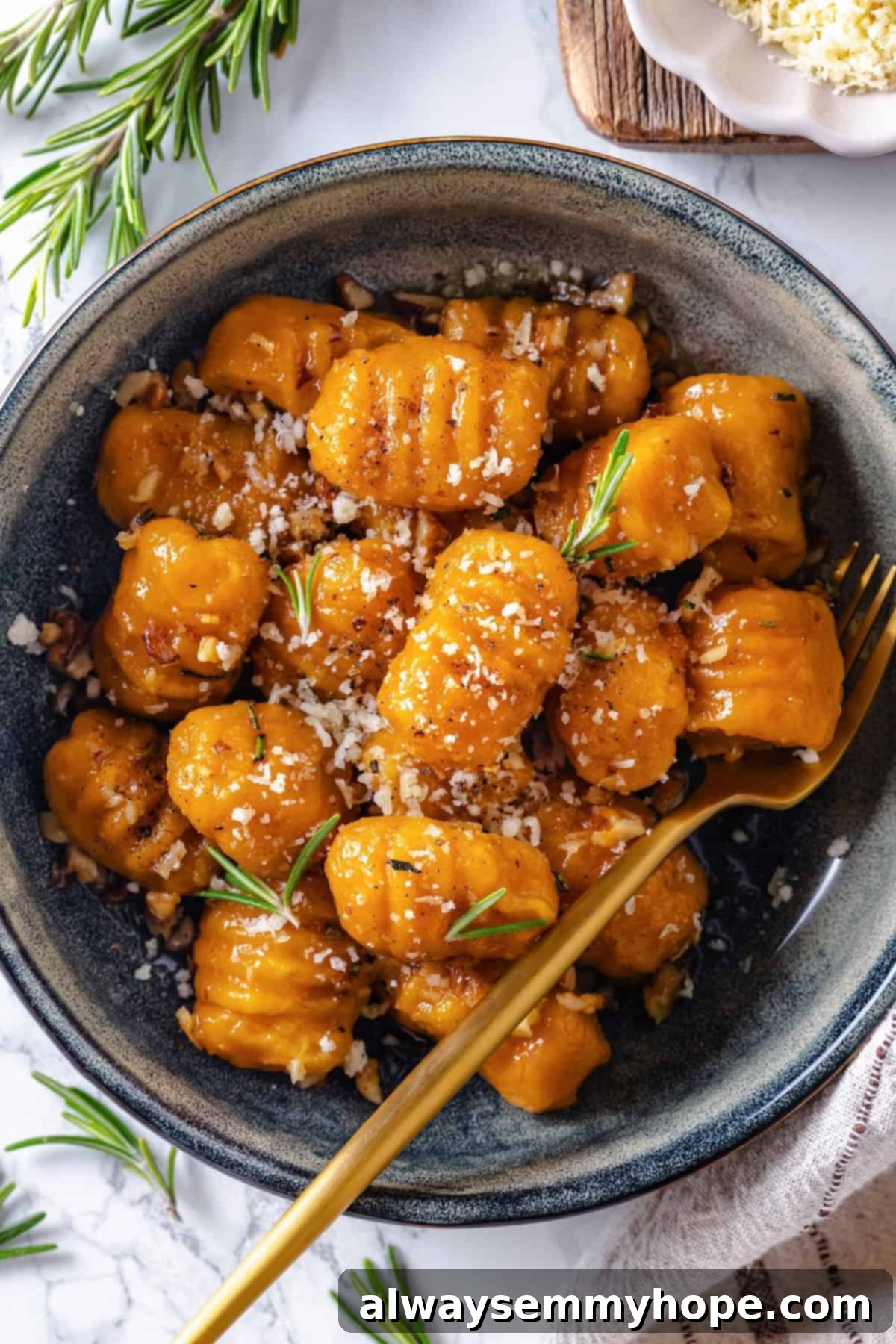 Fork in bowl of sweet potato gnocchi with vegan Parmesan and rosemary.