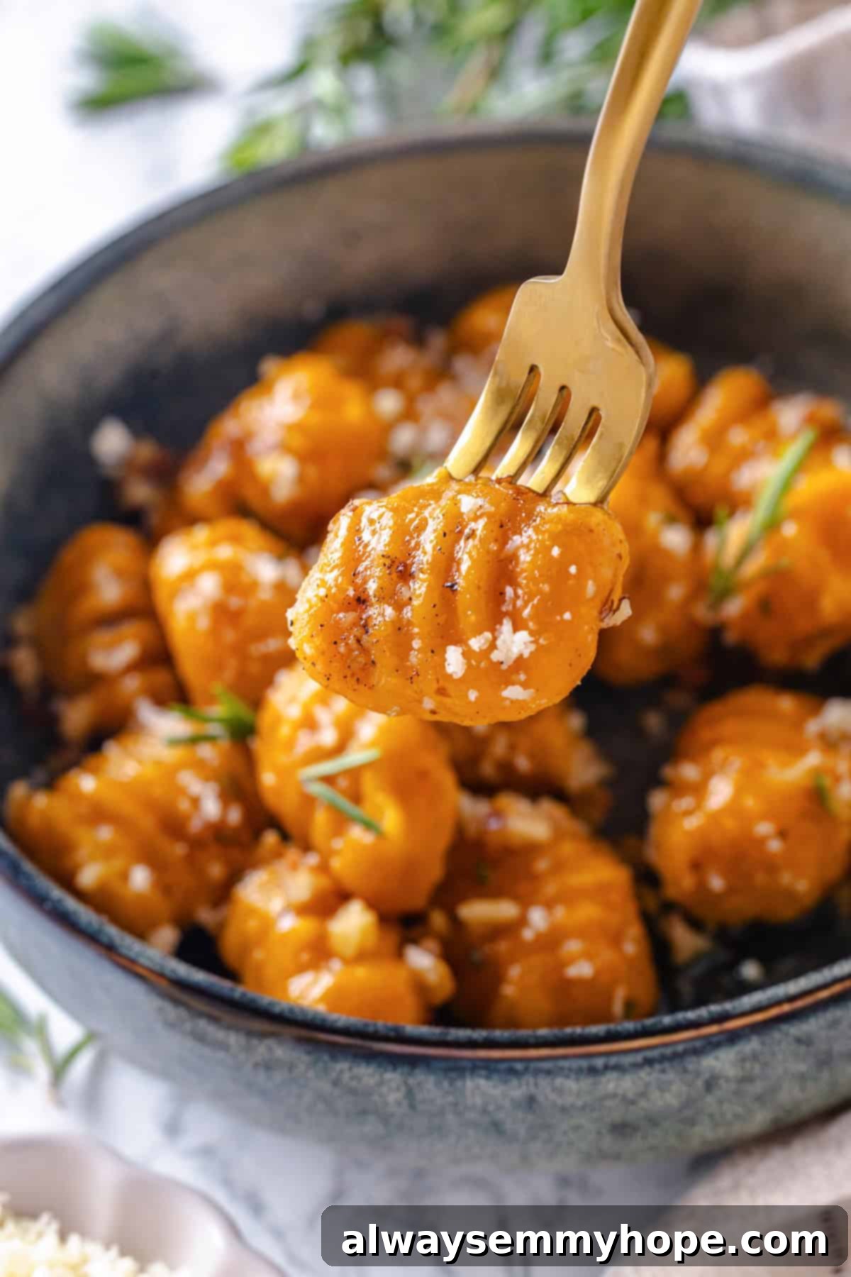 Sweet potato gnocchi on fork with bowl in background.