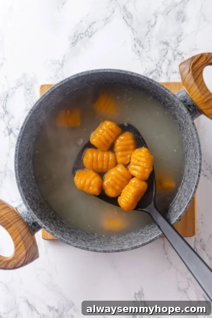 Slotted spoon removing sweet potato gnocchi from boiling water.