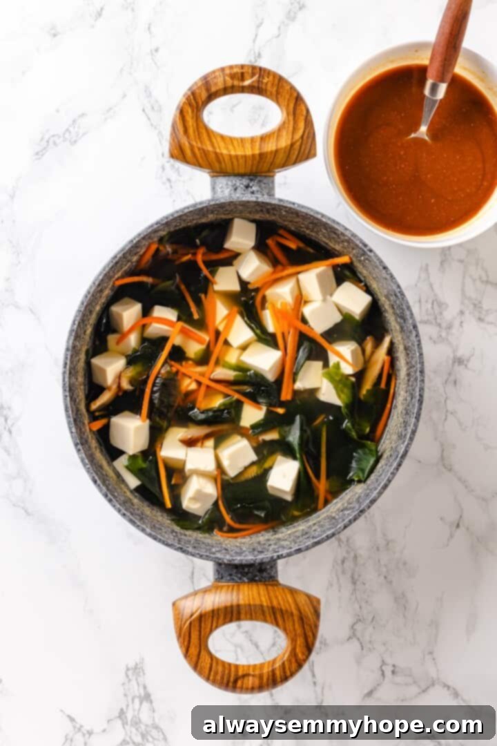 Vegan miso tofu soup set next to bowl of miso and broth mixture.