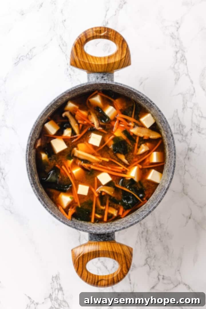 Pot of miso tofu soup with carrots and wakame.