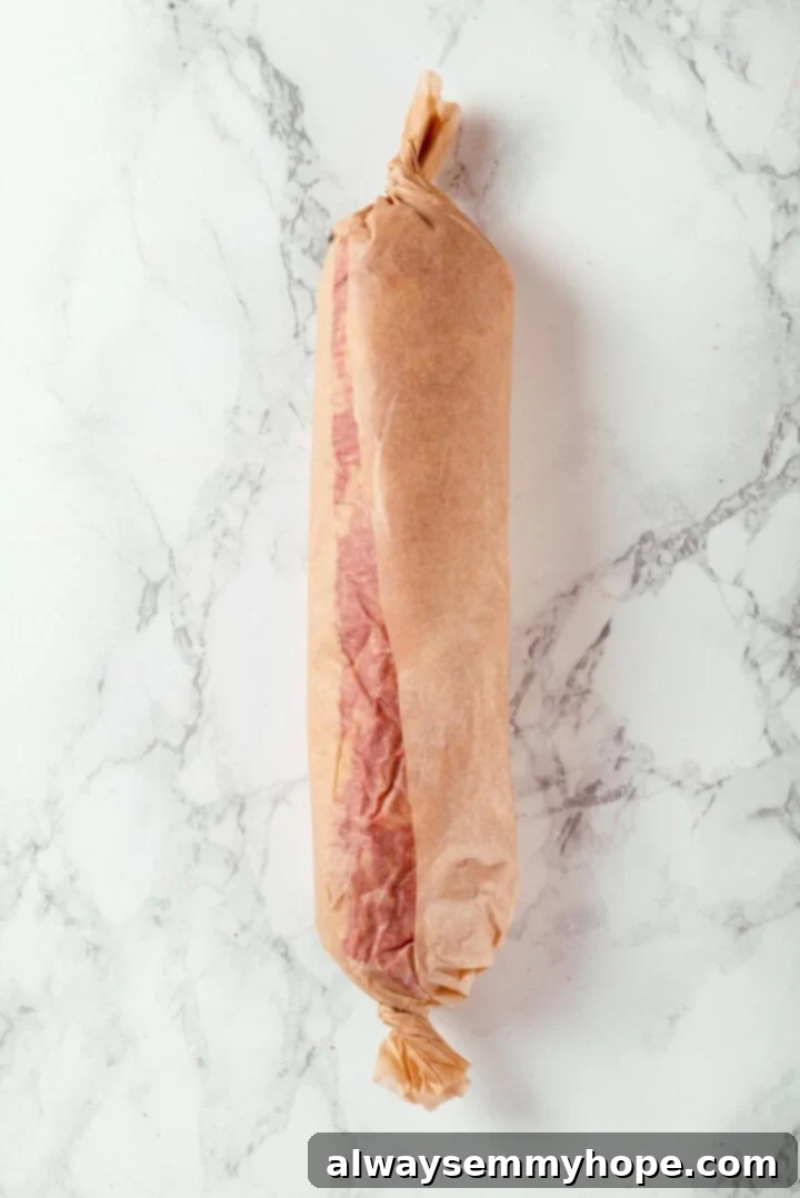 A log of vegan salami wrapped tightly in parchment paper, ready for cooking.