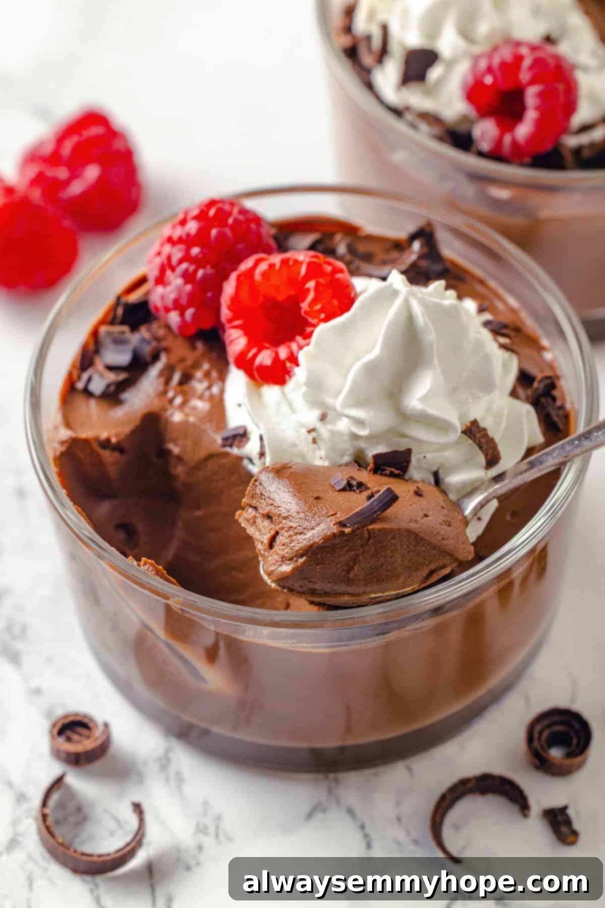 Spoon digging into glass bowl of silken tofu chocolate mousse with vegan whipped cream, raspberries, and chocolate shavings