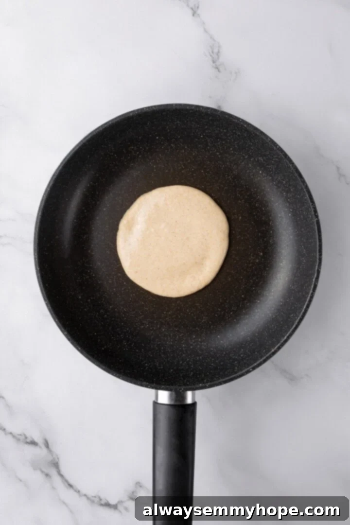 Oat flour pancake cooking in a skillet before flipping.