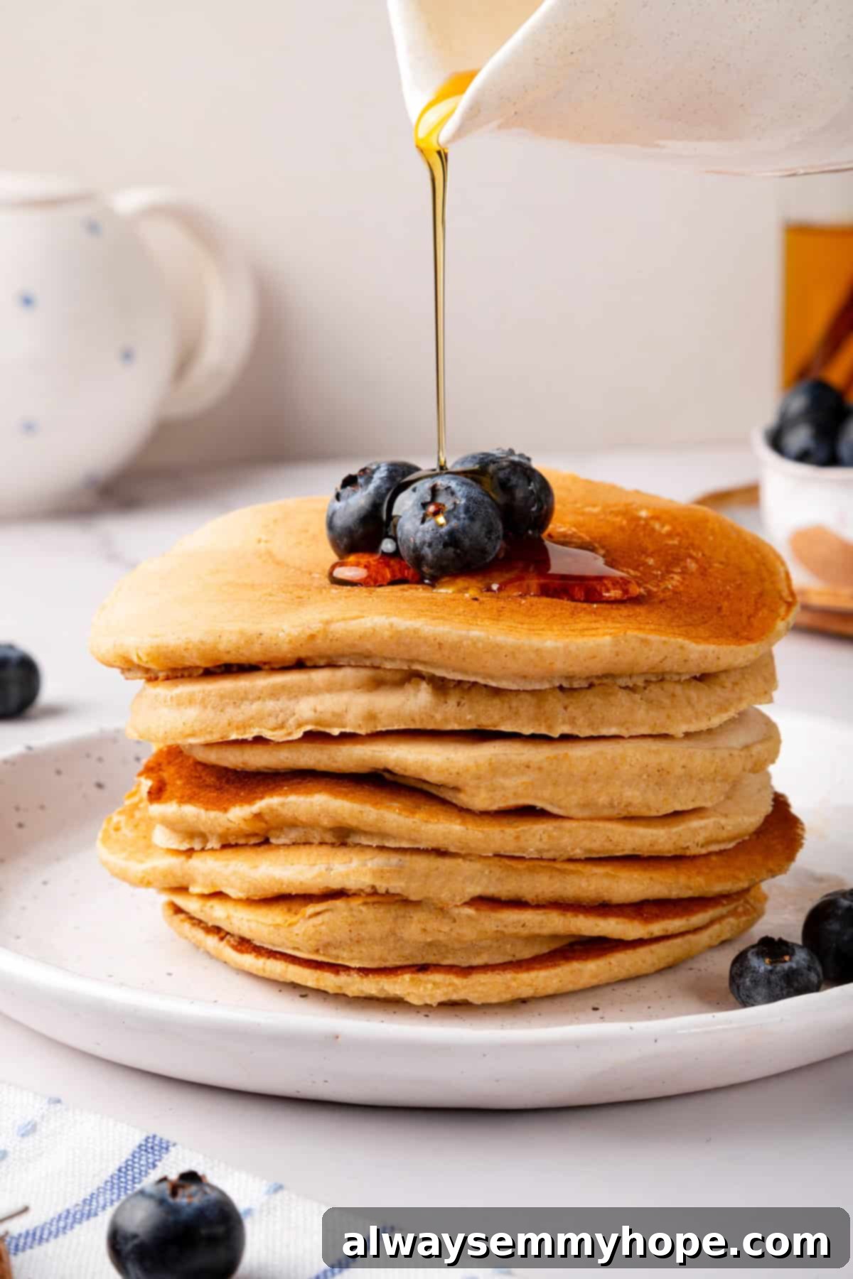 Pouring maple syrup generously onto a stack of oat flour pancakes.