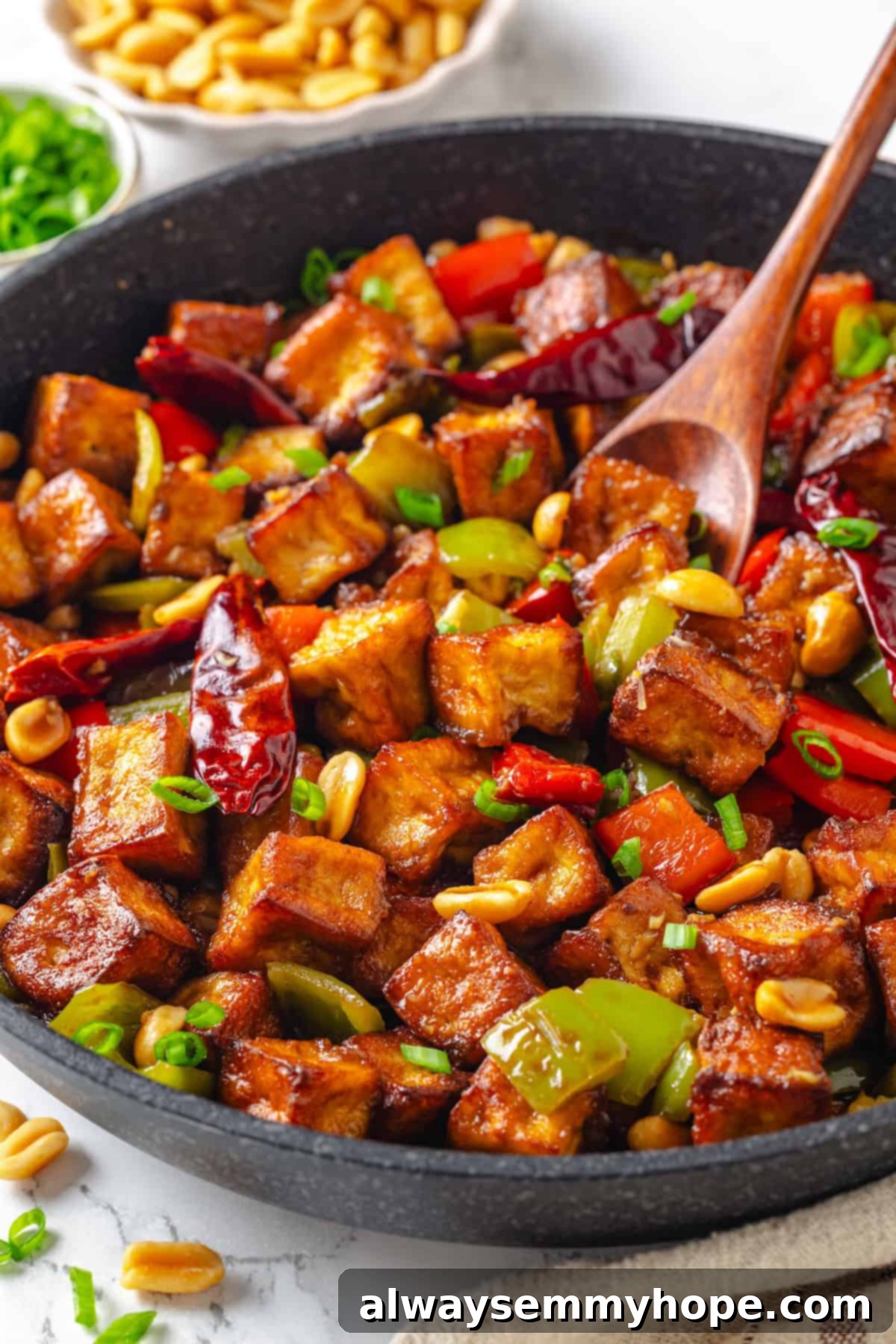 Wooden spoon stirring Kung Pao Tofu in a skillet