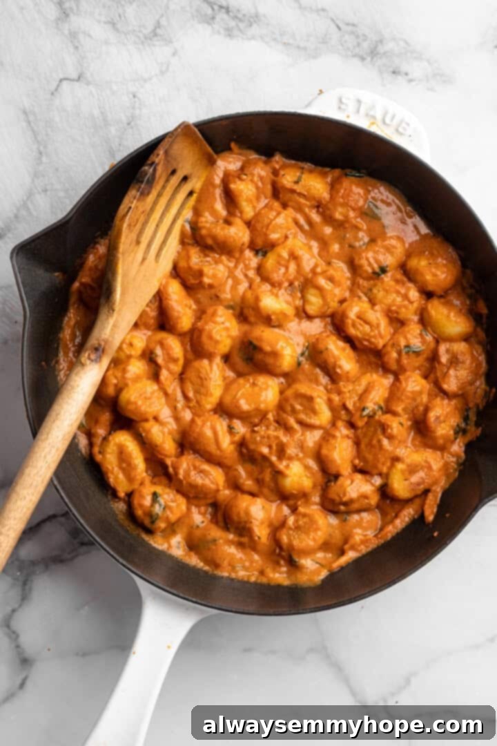 Skillet of cheesy tomato gnocchi with slotted spoon