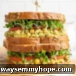 Two smashed chickpea avocado salad sandwiches stacked on cutting board