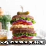 Two stacked vegan tuna salad sandwiches topped with sprouts, lettuce, red onion, and tomatoes